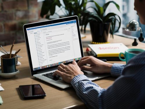 eine Person sitzt an einem Schreibtisch mit einem Laptop und tippt eine E Mail auf Englisch skrivanek