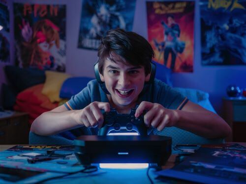 gaming begriffe Ein Teenager sitzt in einem Jugendzimmer am Tisch und beobachtet den Bildschirm, auf dem ein Spiel lauft skrivanek