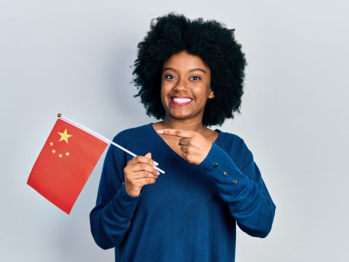 Junge afroamerikanische Frau hält China-Flagge lächelnd glücklich hallo auf Chinesisch Übersetzugnsbüro Berlin Junge afroamerikanische Frau halt China Flagge lachelnd glucklich hallo auf Chinesisch Ubersetzugnsburo Berlin