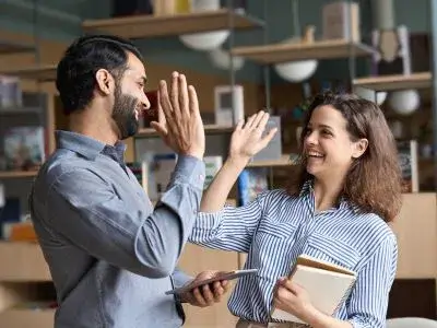 Zwei Kollegen im Buro zeigen ein High Five Emoji in echt lachend und erfolgreich Ubersetzungsburo Berlin Skrivanek